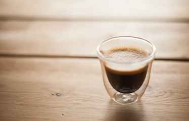 A single shot of espresso in a double wall glass on a wooden table