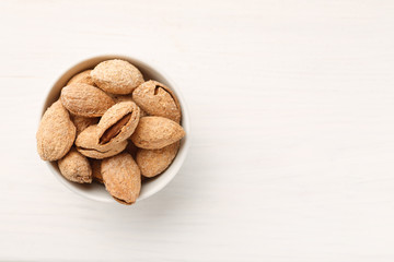 Almond in shell in a white ceramic bowl, top view, copy space