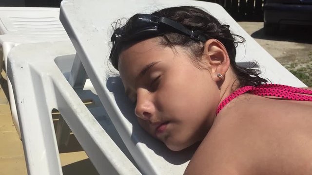 Beautiful young girl teen in swimsuit is lying on chaise-longue near the swimming pool and sleep
