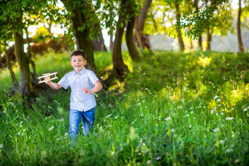 happy little boy is playing with an airplane model in a beautiful evening park