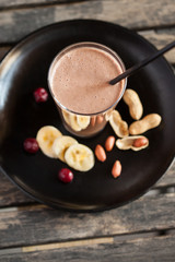 Fresh smoothie with banana, cherry and peanuts on dark wooden table - High angle view