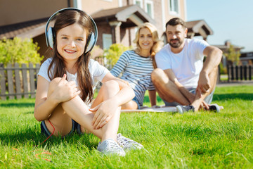 Cute little girl sitting on grass and listening music