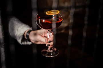 Woman's hand holding a Manhattan Cocktail on dark background.