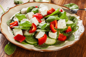 Fresh spinach salad with feta, cucumber and red paprika on a plate.