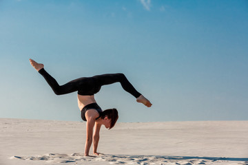 Young woman practicing handstand on beach with white sand and bright blue sky