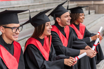 Cheerful graduates relaxing on staircase with diplomas in hands