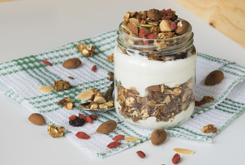 Домашняя гранола с йогуртом в стеклянной банке, на светлом фоне