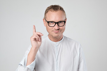 Handsome caucasian young man in white shirt looking at camera and pointing up while standing against white background