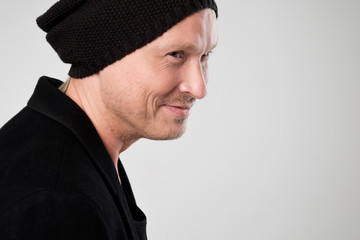 Smiling young man in black clothes standing and hat against white background looking aside