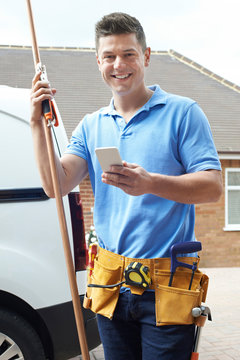 Portrait Of Plumber With Van Texting On Mobile Phone Outside House