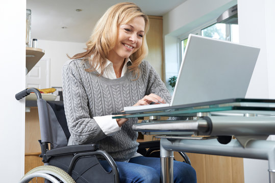 Disabled Woman In Wheelchair Using Laptop At Home