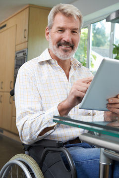 Portrait Of Disabled Man In Wheelchair Using Digital Tablet At Home