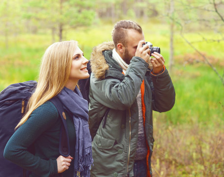 Young beautiful couple walking in forest and taking pictures. Camp, tourism, hiking concept.