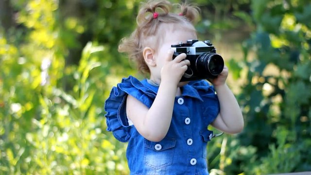 Funny curious baby girl is holding in hands retro камера and photographing in the park. Happy child. Photographer, photosession, photography.