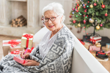 Obraz na płótnie Canvas Cheerful senior woman is holding New Year present