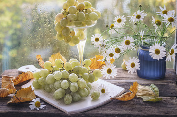 A brush of grapes in a wooden cup, old wooden table white cutting board
