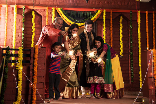 stock photo of Indian Family celebrating Diwali festival with fire crackers with grand parents, young couple and kids in ethnic wear