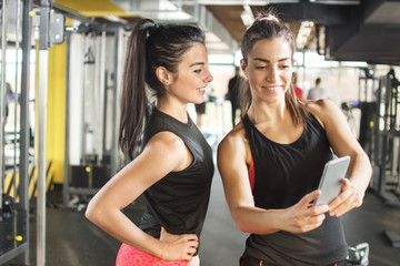 Fototapeta na wymiar Two sporty girls looking something on mobile phone in gym.