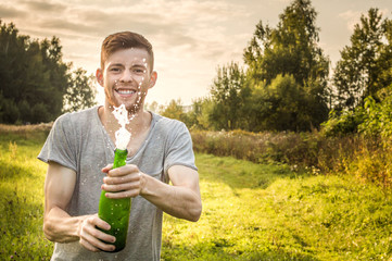 Fototapeta premium the young man opens a champagne bottle in the park