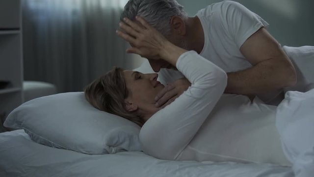 Aged couple lying in bed and caressing each other, man kissing woman hand, love