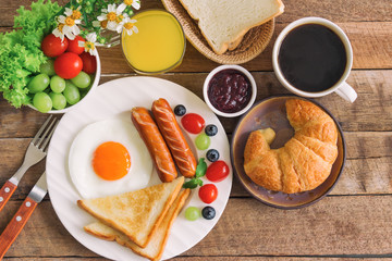 Homemade breakfast with sunny side up fried egg toast sausage fruits vegetable croissant strawberry jam black coffee and orange juice in top view flat lay concept.Delicious homemade american breakfast