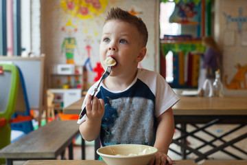 Cute toddler boy eating in indoors cafe