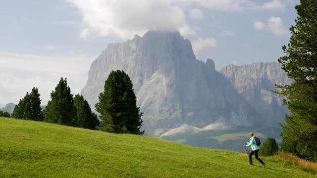 Woman hiking along the green slope agains the backdrop of mountains