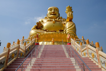 Sculpture assise du grand Bouddha doré, tenant des barres d& 39 or à la main, sur une colline en haut des escaliers avec fond de ciel en Thaïlande.