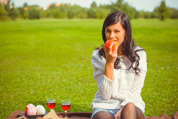 A young woman with dark hair in a white sweater at a picnic is resting on the green grass and is having a rest this afternoon. Beauty of nature and relax at sunny day