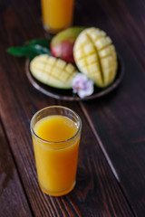 Fresh tropical mango juice on table with mango fruits on background.