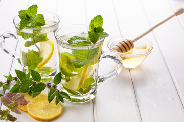 Two glass cups fresh mint tea with lemon and honey on white background.