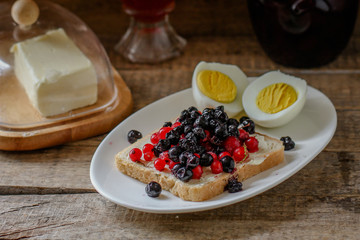 light breakfast (snack) a sandwich with blueberries and red currants, boiled eggs - in rustic style on a wooden surface 