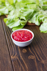 Mexican salsa or indian chutney in white ceramic bowl against green herbs