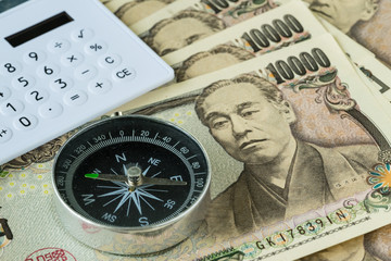 Compass and calculator on pile of japanese yen banknotes as financial safe haven or tax concept