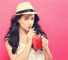 Happy young woman drinking smoothie on a pink background