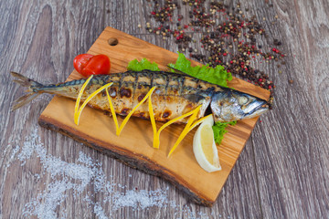 Mackerel baked on charcoal, on a wooden board with lemon and lemongrass