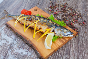 Mackerel baked on charcoal, on a wooden board with lemon and lemongrass