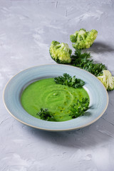 Vegetarian vegan broccoli cream soup served in blue plate with fresh parsley and broccoli over gray concrete background. Copy space. Healthy eating.