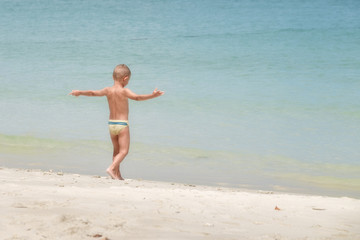Fototapeta premium European boy age 3-5 years old stands on the beach, Opening arm.5 years old stands on the beach, Opening arm.