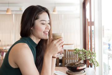 Young happy Asian woman drinking coffee in the coffee shop.