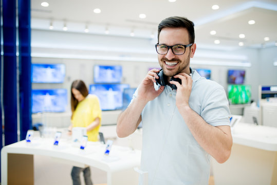 Charming happy man is testing new headphones in the electronics store.