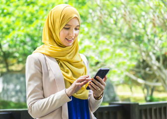 Happy young muslim woman messaging on a mobile phone in the park - 171210967