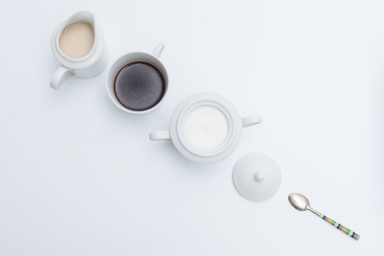 Vista cenital de juego de cafe, lechera, azucarero y cucharilla con fondo blanco