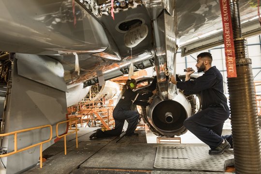 Aircraft maintenance engineers examining turbine engine of