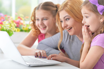 Mother and  girls sitting at  table and using  laptop