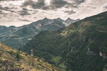 Sunlight on alpine valley with glowing mountain peaks and scenic clouds. Italian French Alps, summer travel destination, toned image, vintage filter, split toning.
