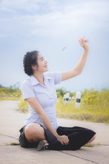 The asian girl is smiling on the road in the meadow and the umbrella and looking at the grass flowers in her hand