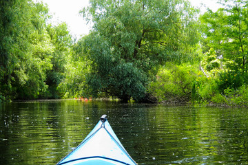Bow of blue kayak. View over lake with green trees from blue kayak. Kayaking in calm spring day. Reserve on Danube river delta