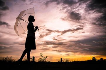 The girls silhouette style walking alone outdoor and umbrella in her hand with cloudy skies and evening sun
