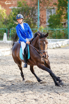 Young girl on bay horse galloping on her course on show jumping competition